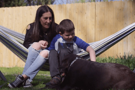 Woman and son sitting in hammock petting service dog