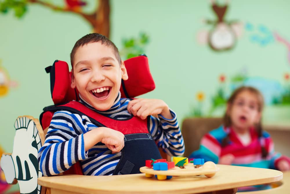Child in wheelchair smiling in classroom. 