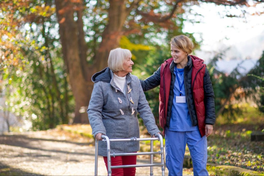 A caregiver and elderly woman walking outside 